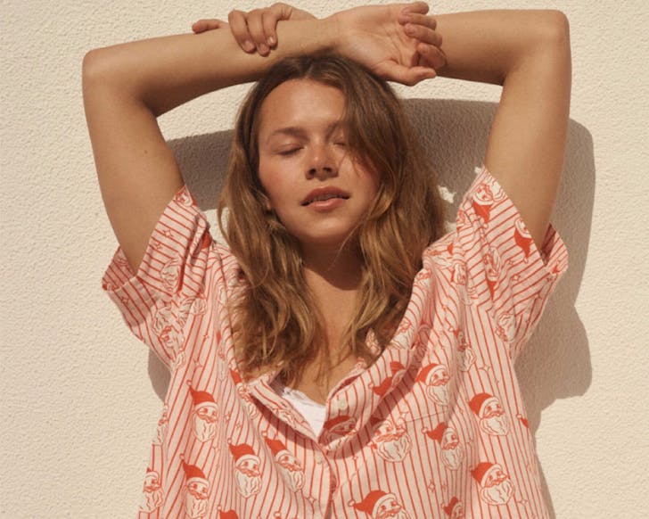 Woman wearing a red stripy pyjama top with a Santa head print closes her eyes with her arms crossed over her head. 