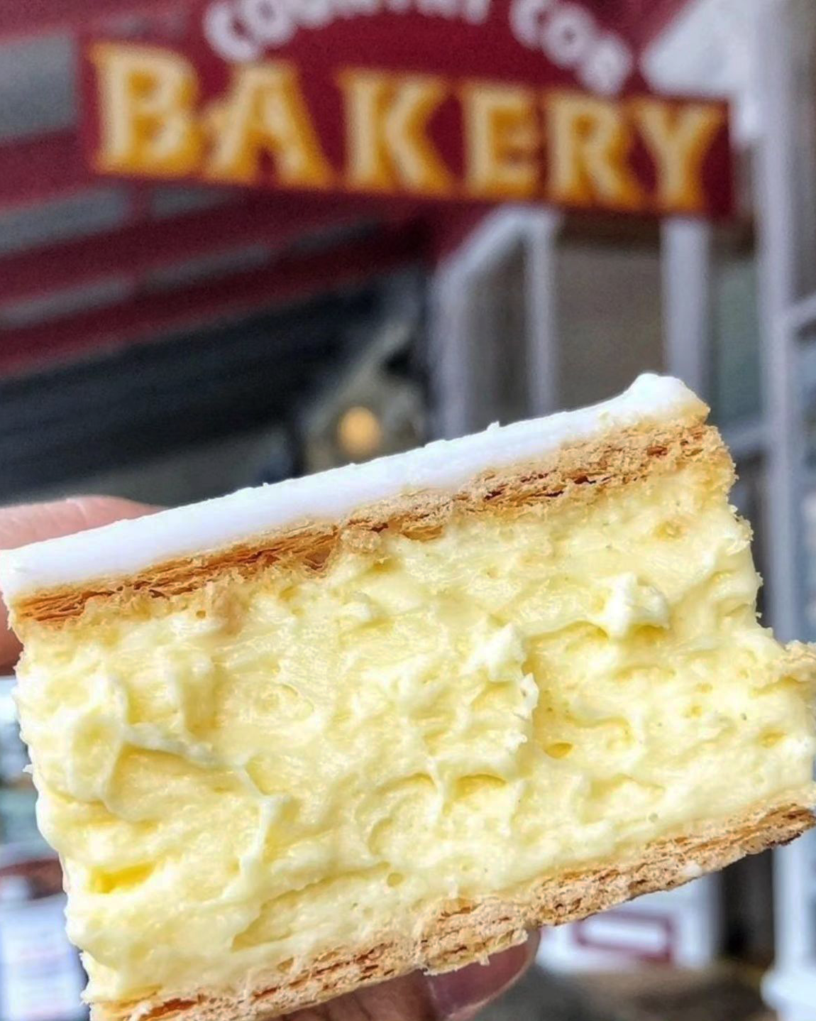 A person holding up an award-winning vanilla slice melbourne out front a bakery.