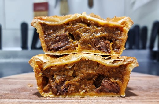 Two pies that have been sliced open showing the chunky beef filing and golden pastry.