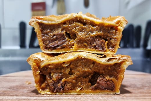 Two pies that have been sliced open showing the chunky beef filing and golden pastry.