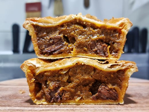 Two pies that have been sliced open showing the chunky beef filing and golden pastry.