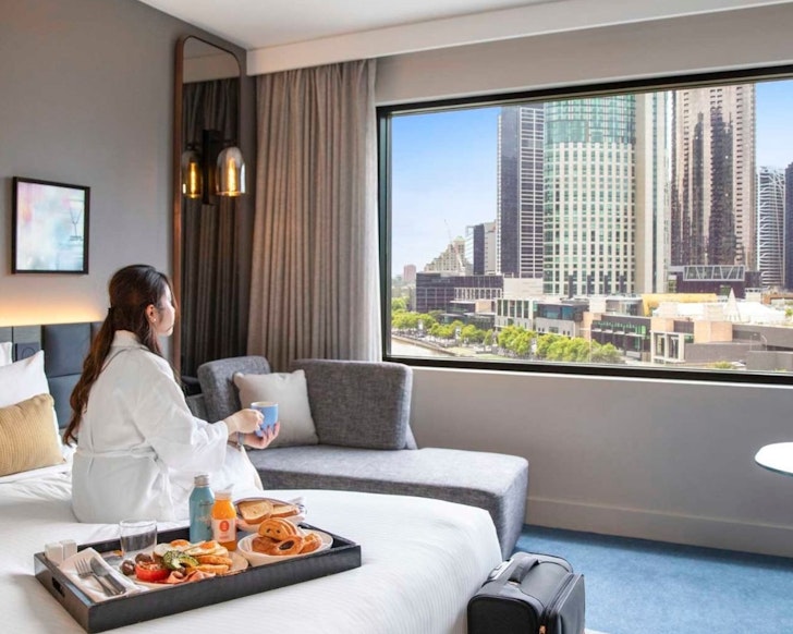 A woman sits on a bed looking out of the window at Crown Plaza Melbourne one of the best hotels for the British and Irish Lions Tour