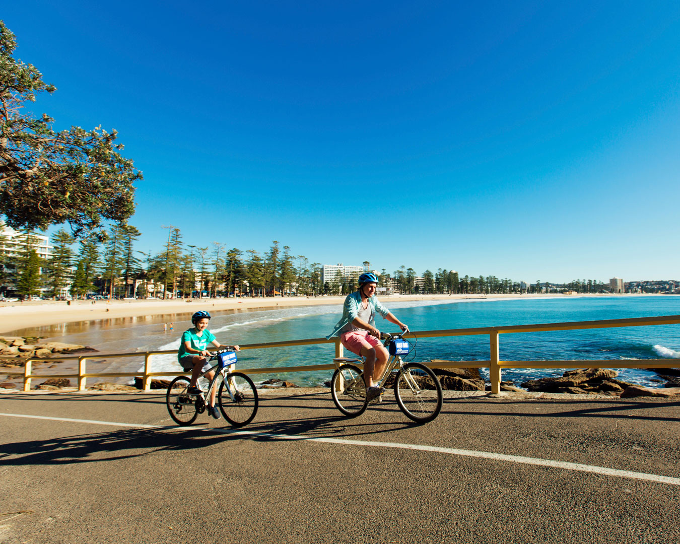 Two people cycling by Manly Beach