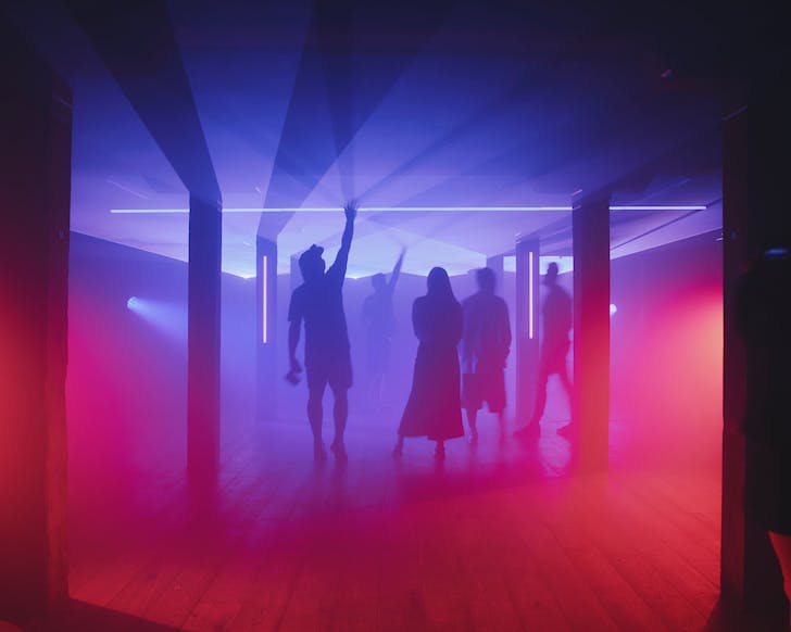 A group of silhouetted people enjoy a pink and purple-lighted DARK audiovisual experience.