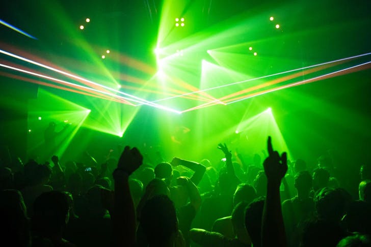 the silhouette of a crowd at a music concert with green laser lights
