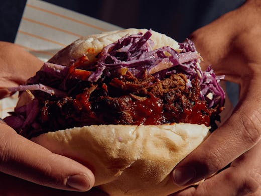 Two hands holding up a roll filled with red cabbage and pulled pork. 