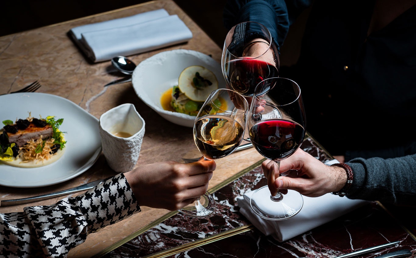 3 wine glasses cheers over a dinner table, dimly lit