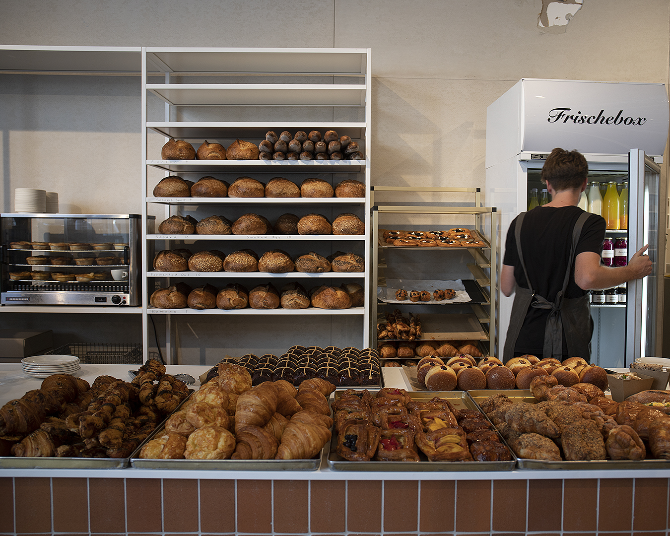 A server dives into the chiller cabinet at Daily Bread with an array of delicious baked goods in the foreground.