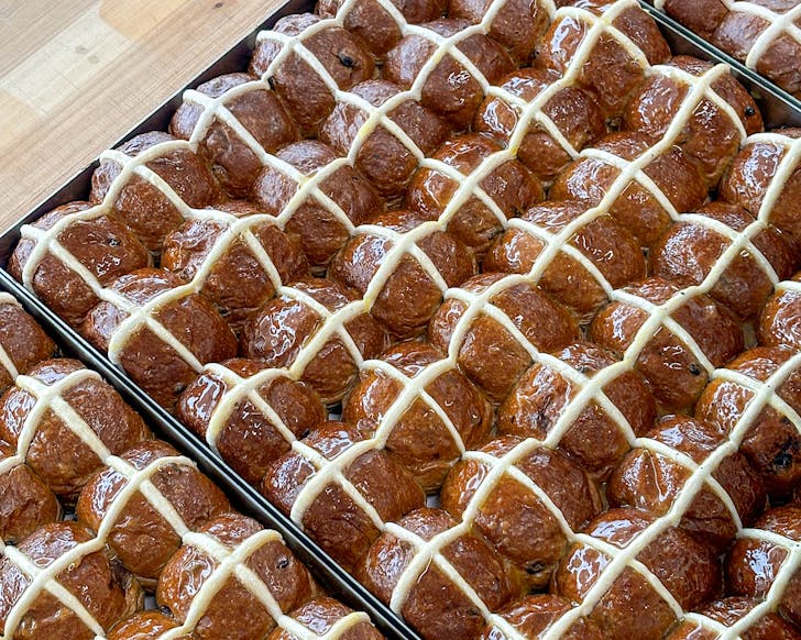 Three trays filled with freshly-piped hot cross buns. 