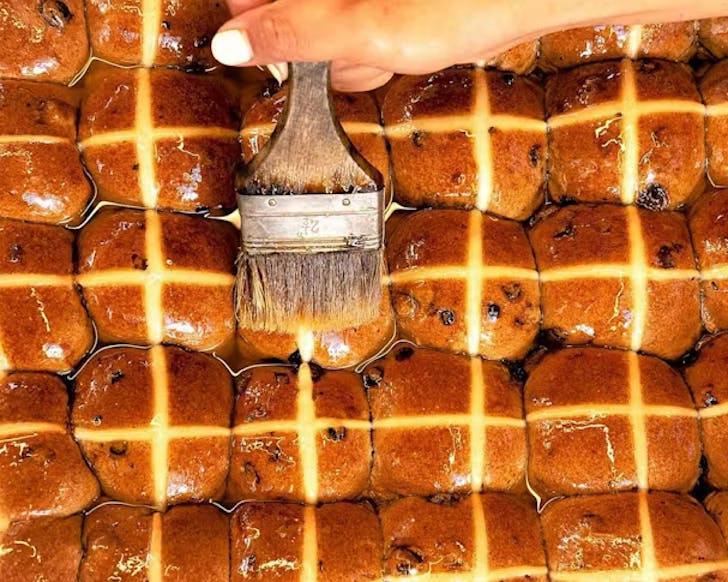 Someone paints a glaze on a whole lot of Daily Bread hot cross buns. 