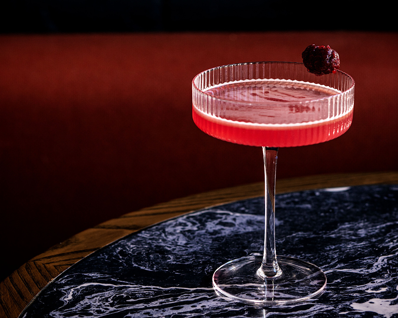 An elegant, ridged cocktail glass filled with a bright red liquid sits on a black marble bench at Daphne’s Bar Taverna. 