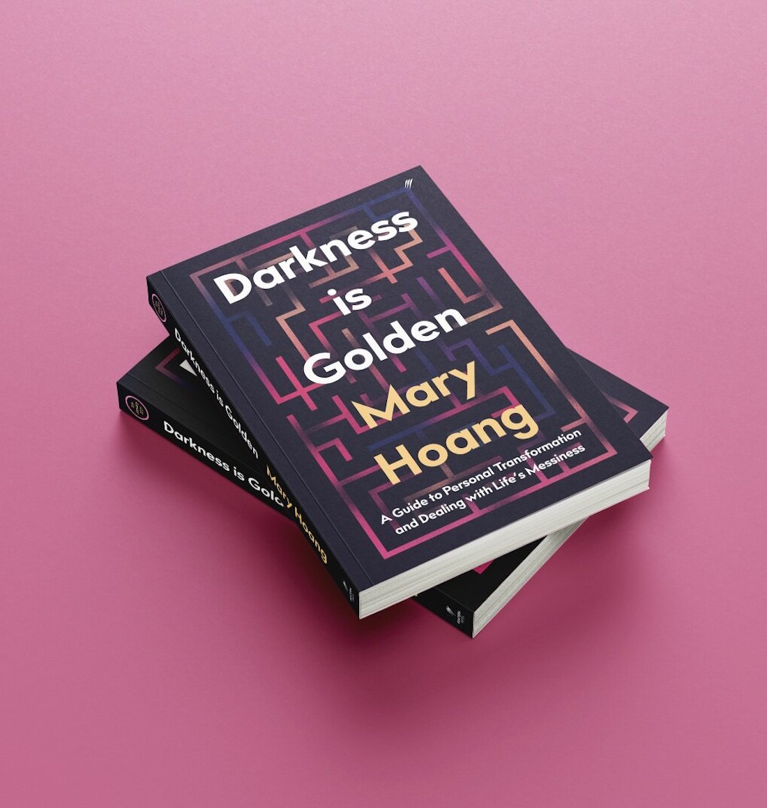 Two books lie stacked on top of eachother against a pink background.