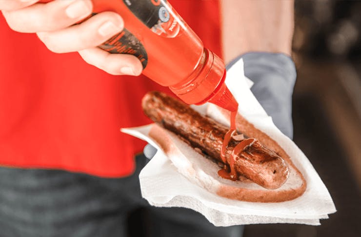 A person putting sauce on a sausage.