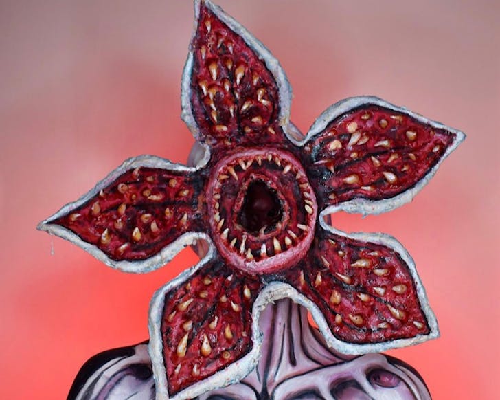 A person dressed up for Halloween in an impressive handmade demogorgon costume with a massive red flower head opening up to rows and rows of sharp teeth. 