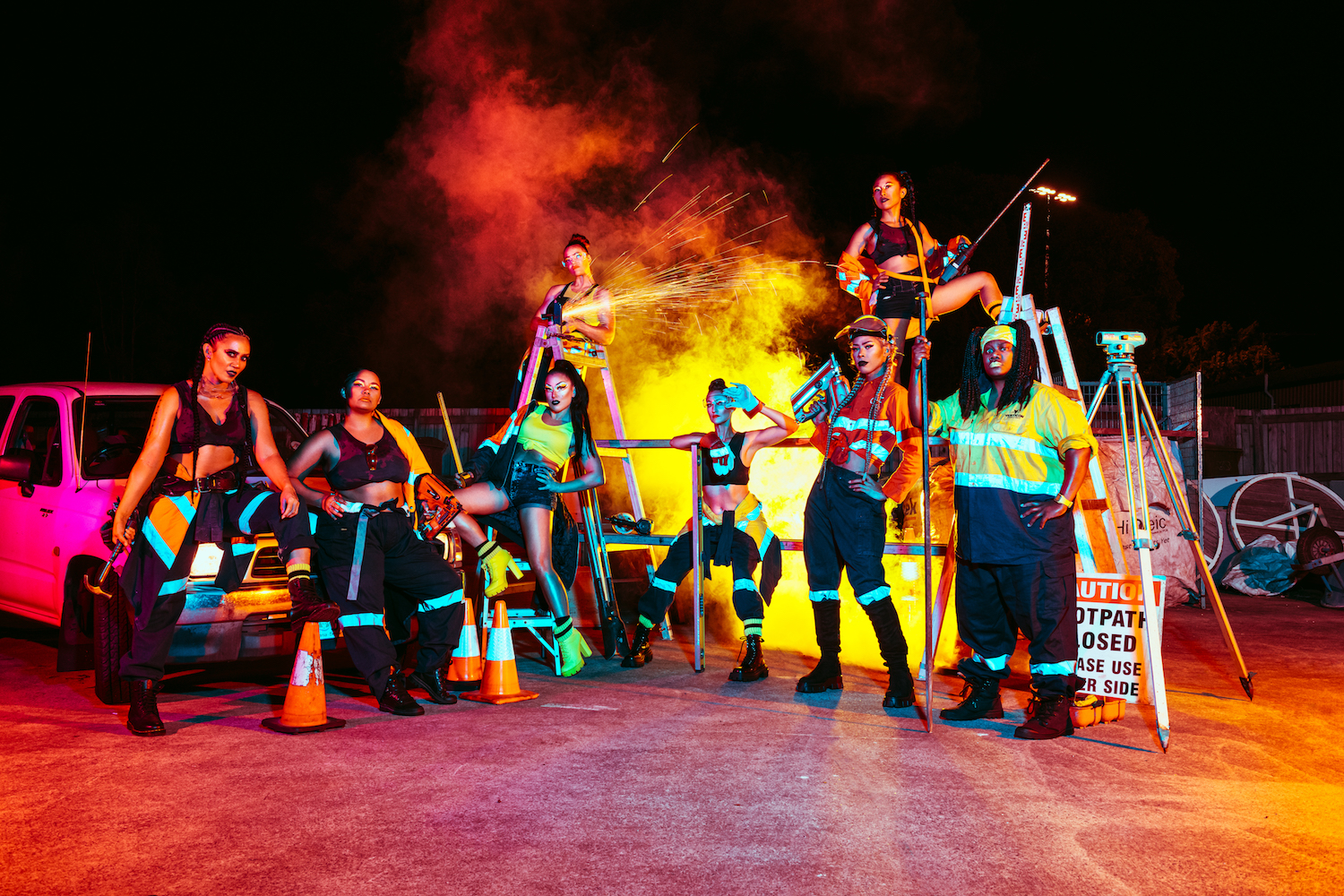 A group of tradies stand on stage posing around ladders and fire.
