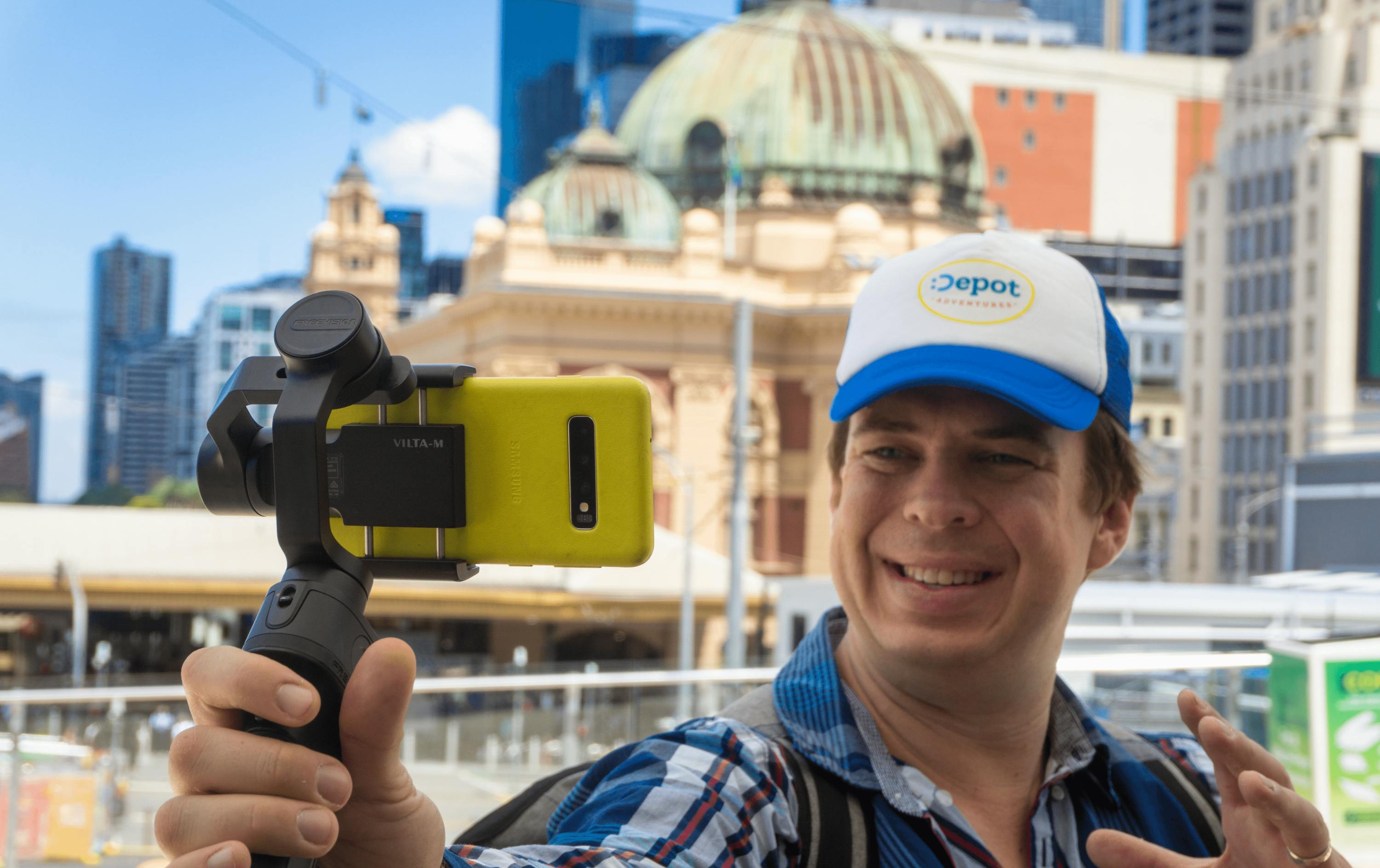 A man holding up a phone out front Flinders Station. 