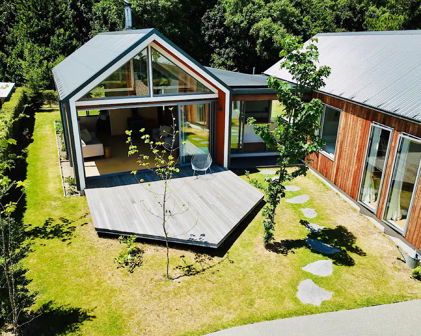 A glass-front home wraps around a pentagon-shaped deck and lawn area with several intriguing trees. 