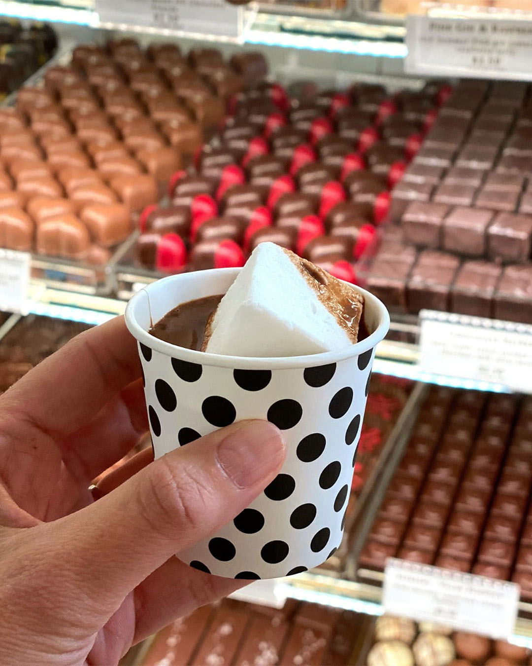 A hot chocolate shot with a vanilla marshmallow is seen in front of rows of handmade chocolates at Devonport Chocolates.