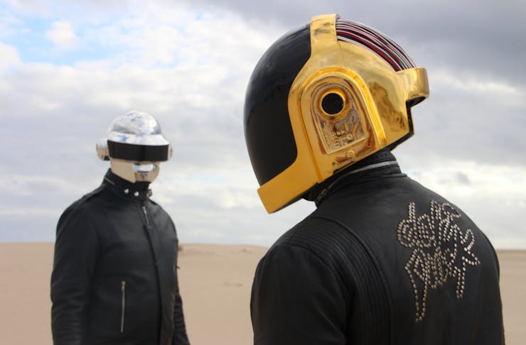 Discovery Tribute Band stand in the desert with helmets on.