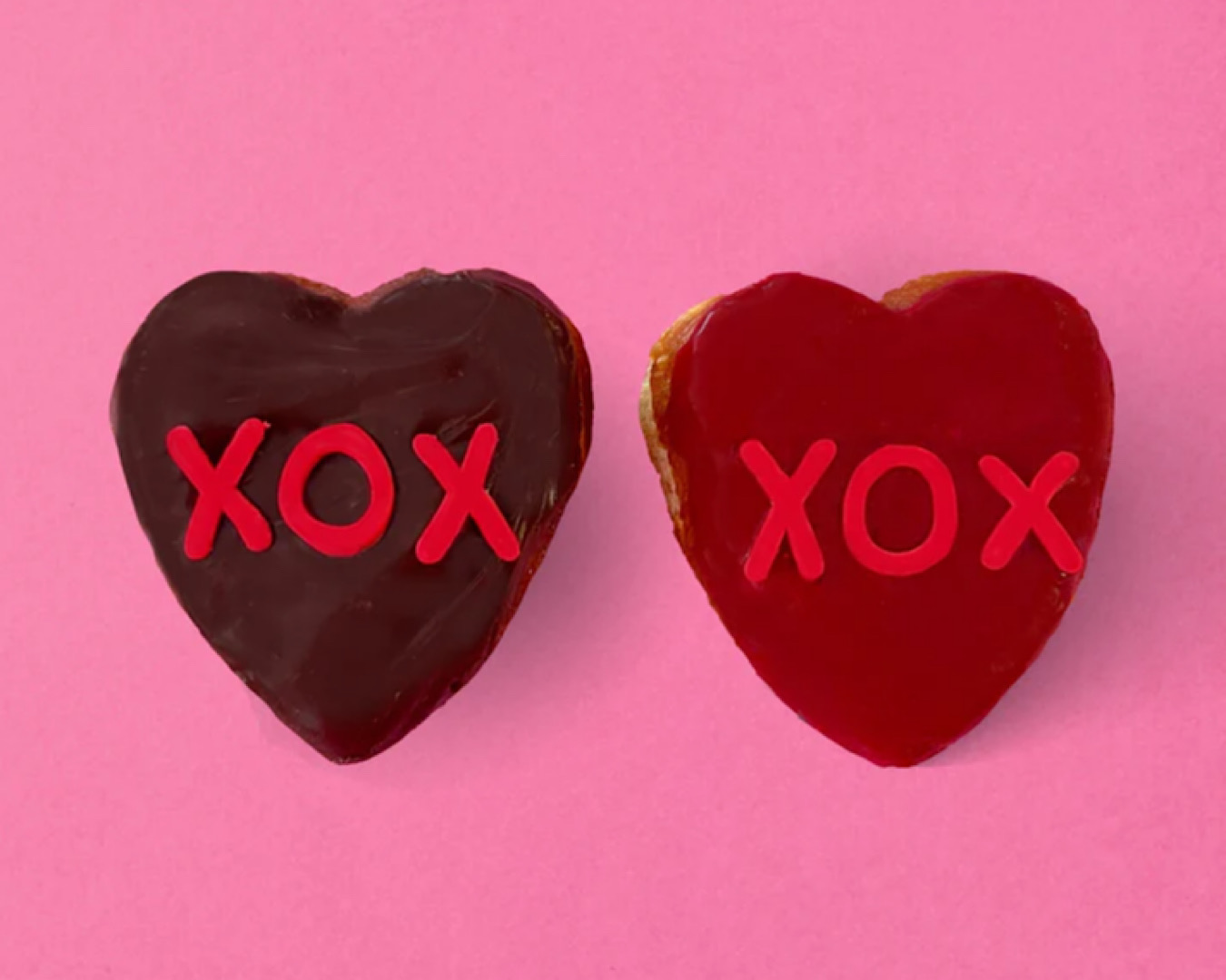 Two heart-shaped donuts-one red, one brown-with XOX written on them in icing. 