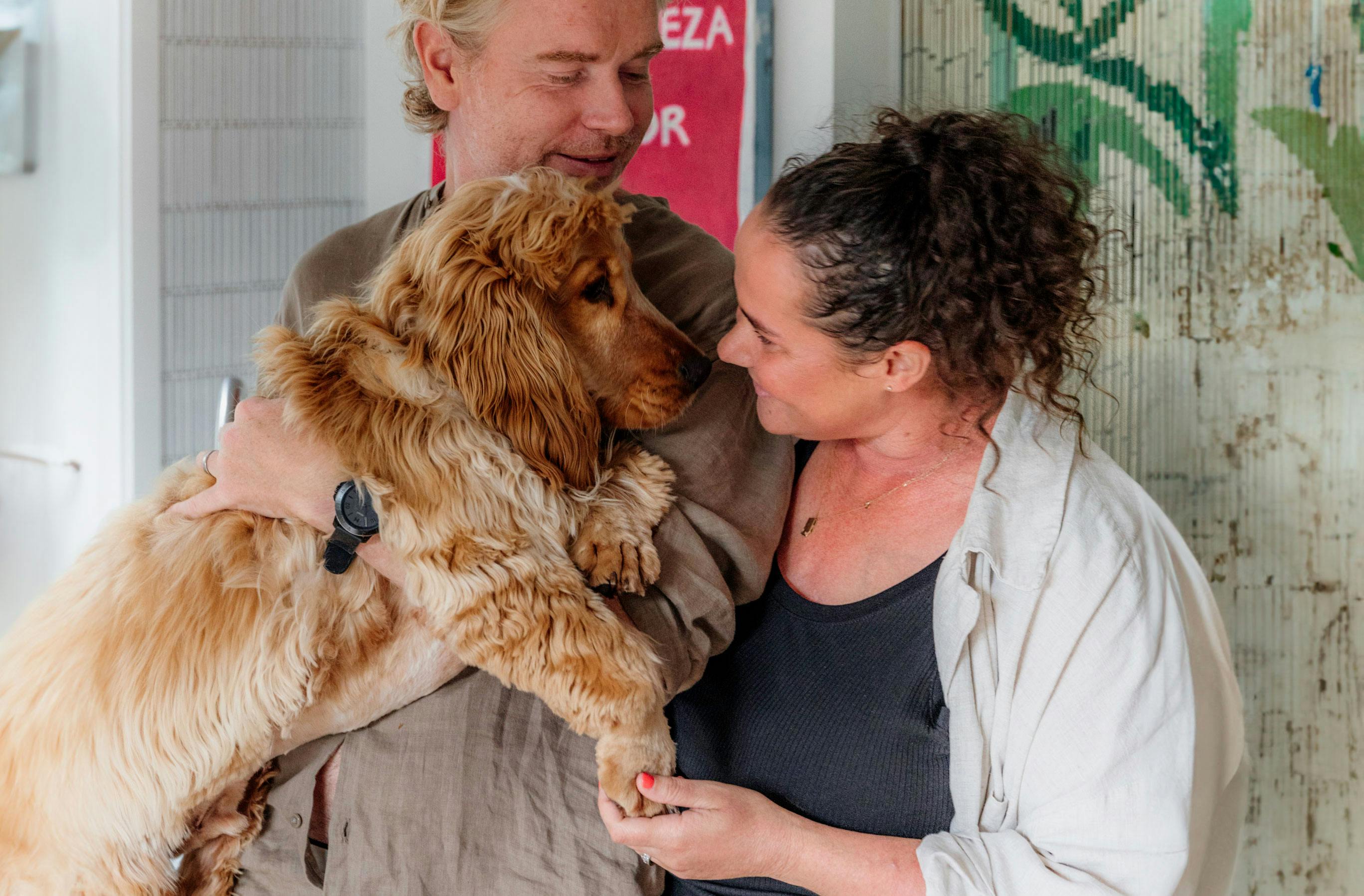 Couple smile and hold up their dog in their home