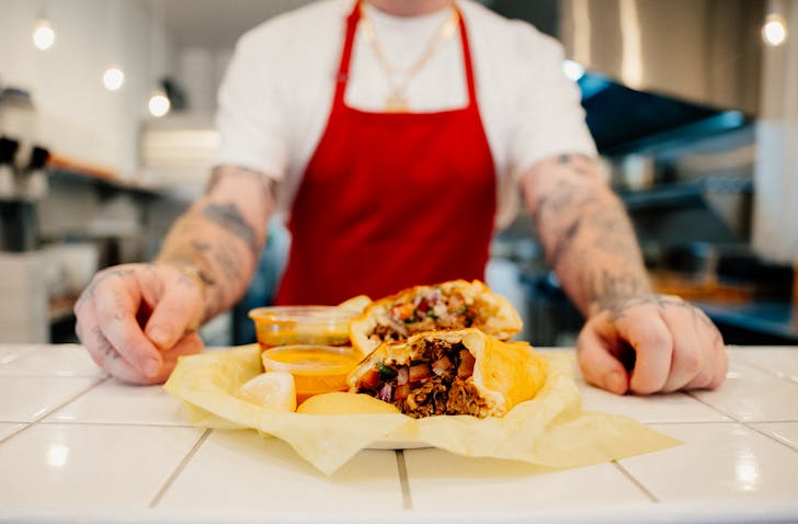 Sean Yarbrough stands behind a brand new DoorDash-only birria chicken burrito with orange sauce. 