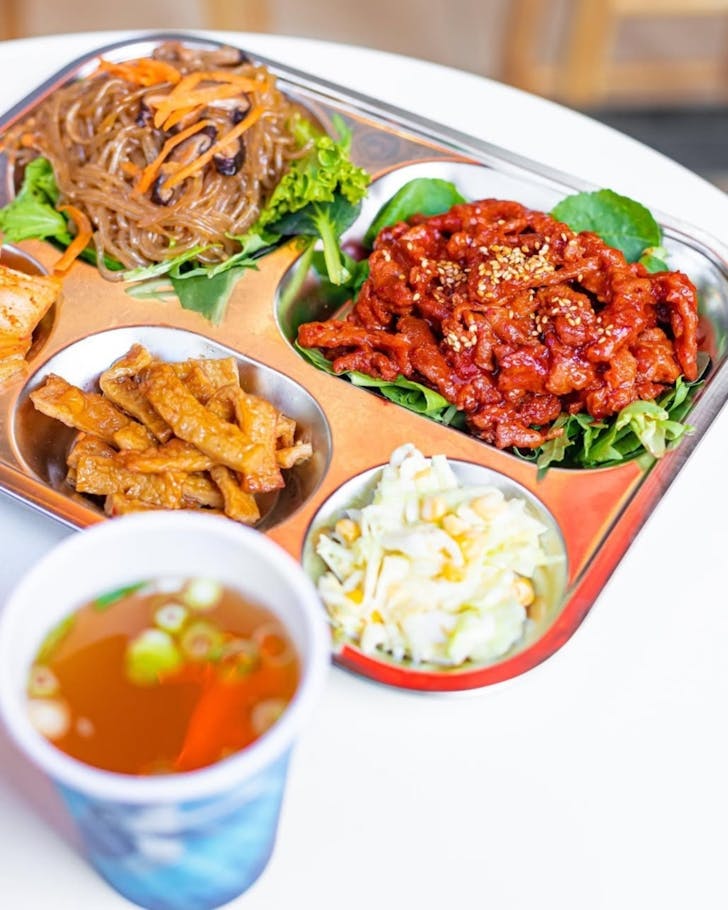 Korean lunch trays featuring rice, side dishes and protein.