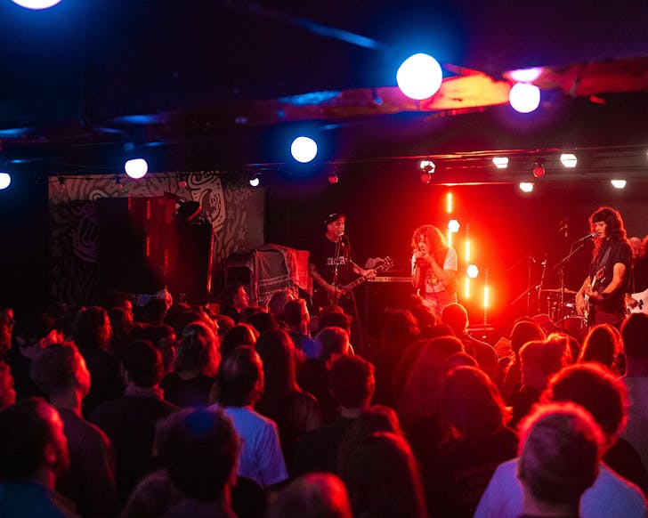 A live gig packed with people in a basement and bathed in red light.