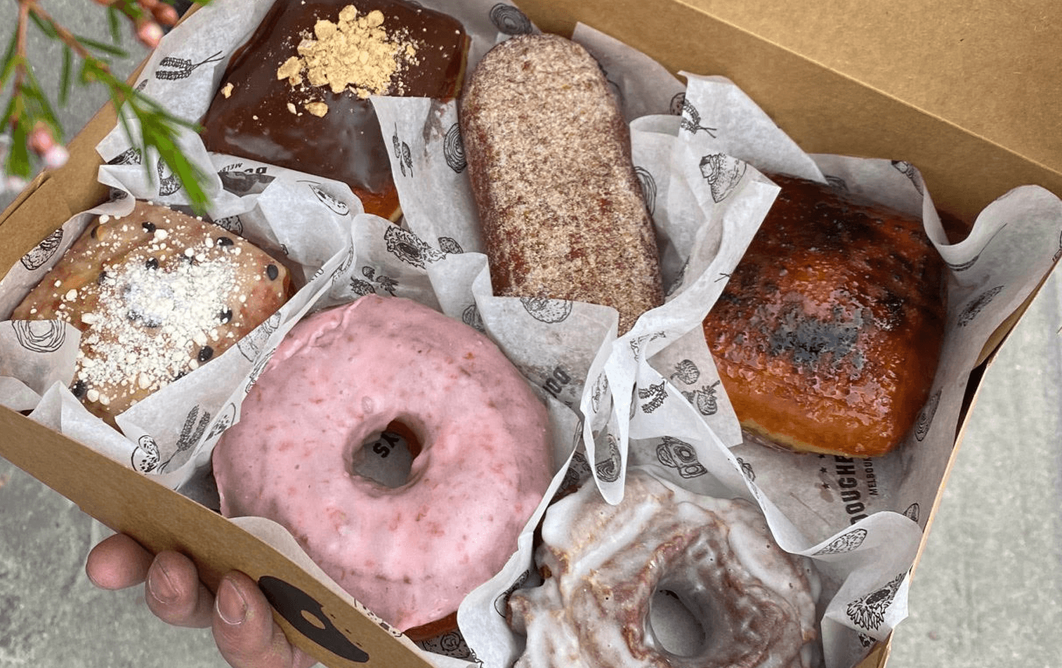 A tray with pink, chocolate and elongated donuts of Melbourne. 