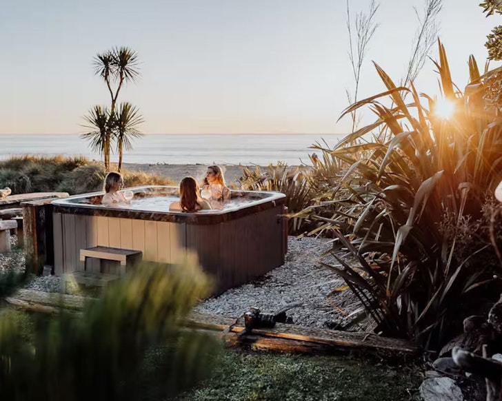 Friends relax in the outdoor hot tub at Drifting Sands Beachfront Retreat one of the best beach house Airbnbs NZ
