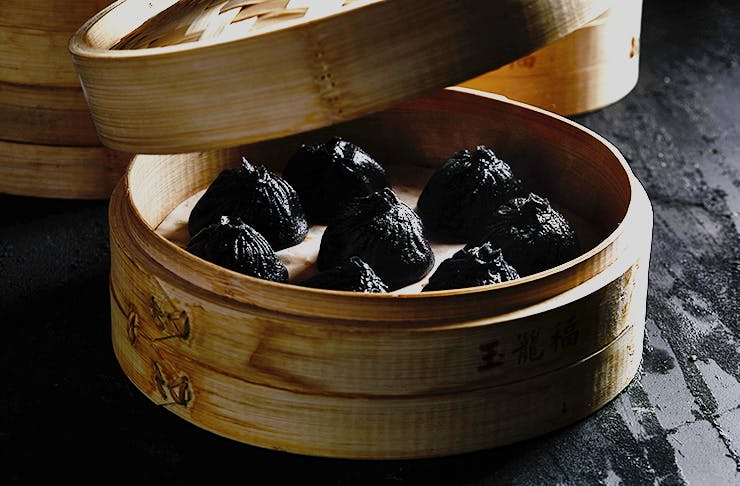 Black dumplings sitting inside a bamboo dish. 
