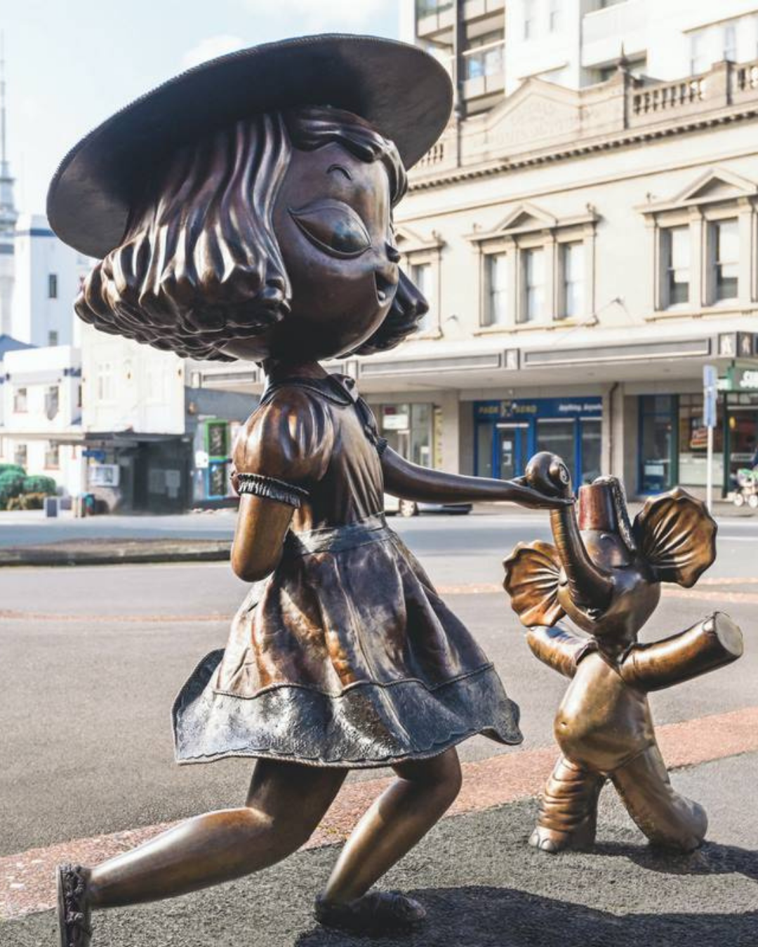 Two small bronze sculptures on Karangahape Road of a girl holding hands with an elephant.