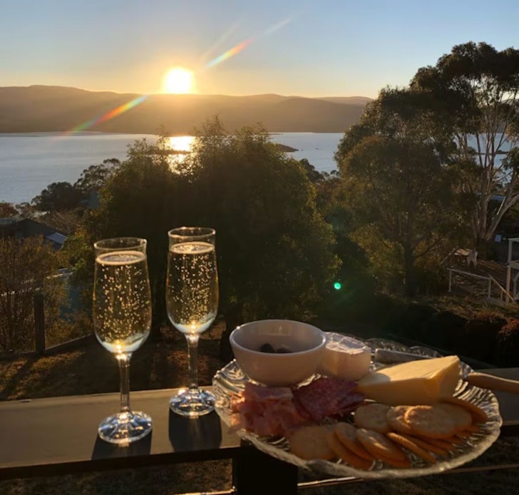 Two champagne glasses sit on a table overlooking the water at EJ's B&B one of the best accommodation options for solo travellers in Jindabyne