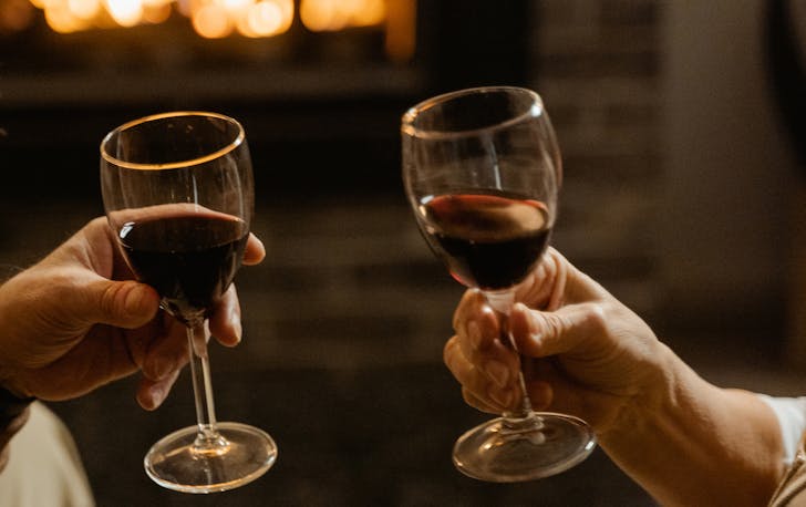 Two glasses of red wine held in front of a fireplace