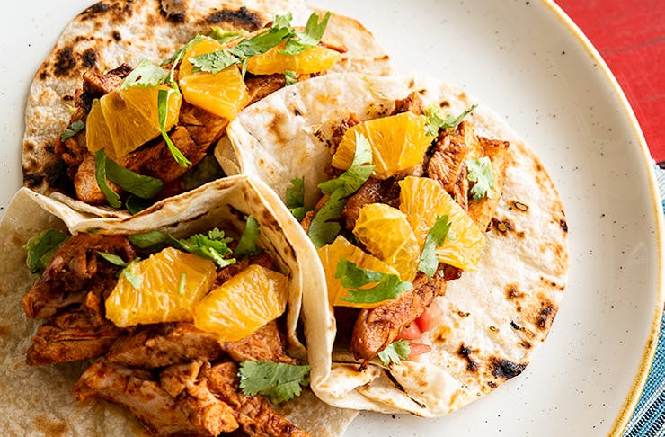 Three soft shell chicken tacos topped with mandarin pieces.