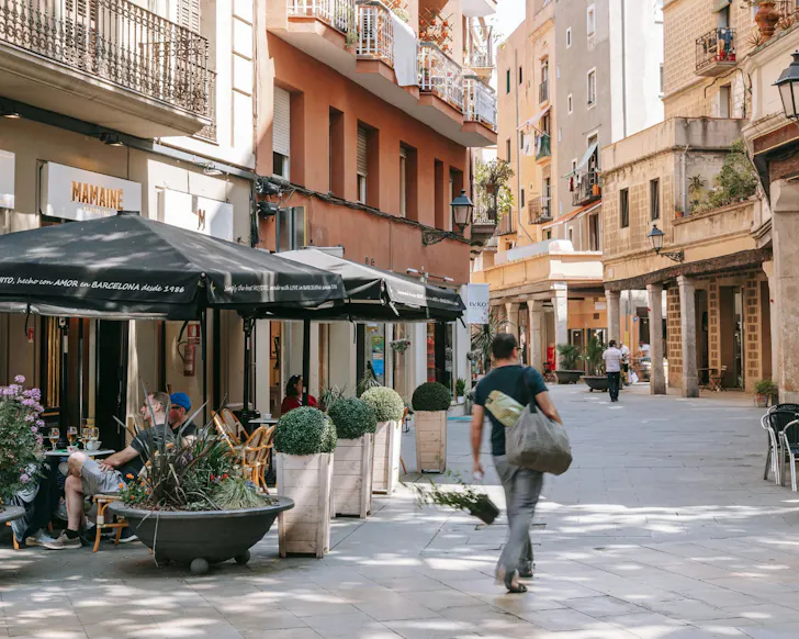 A man walks down a cozy, light-filled street filled with cafes and shopfronts in El Born, Barcelona. 