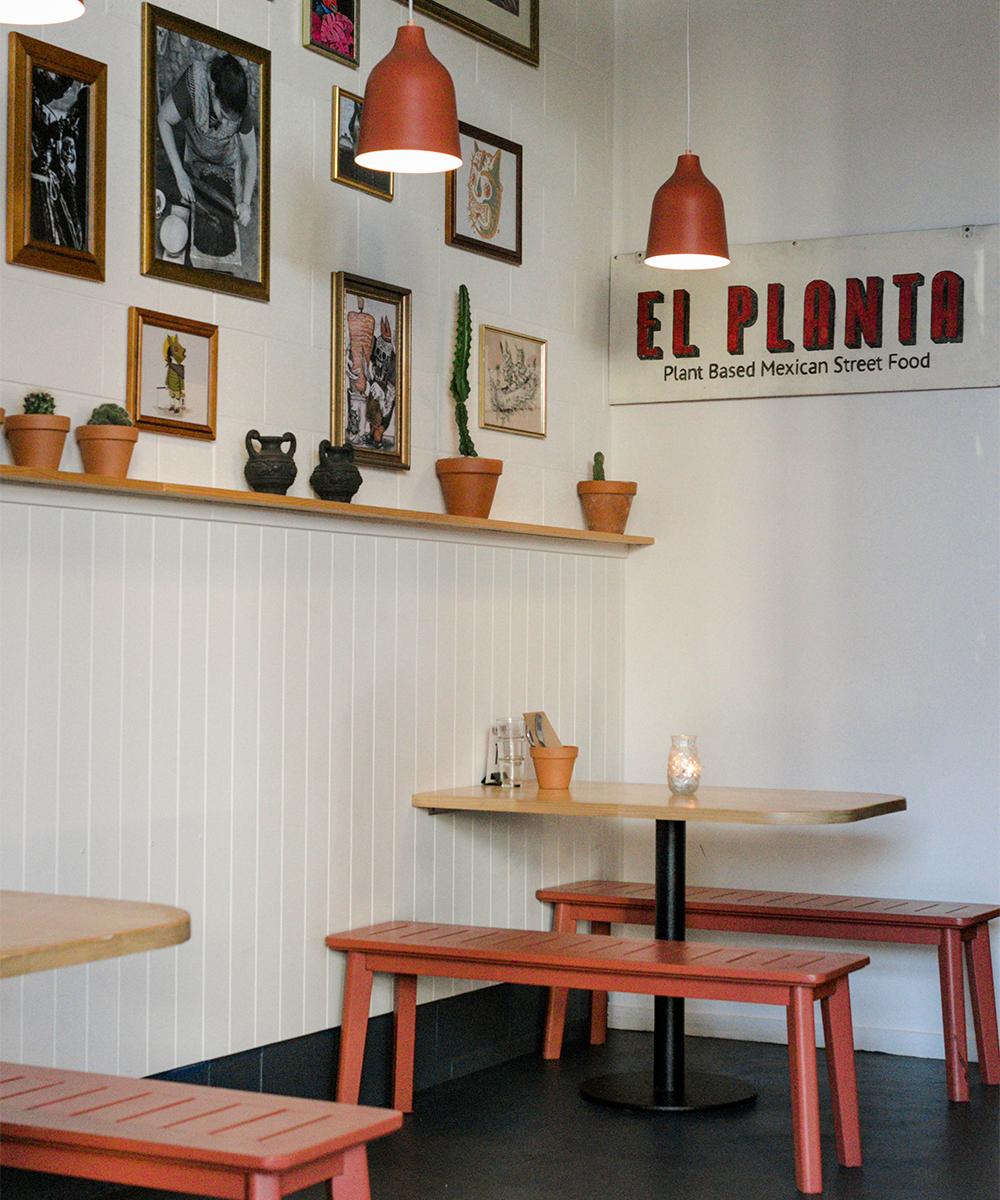 Interior of El Planta, with two red tables along a frame covered wall