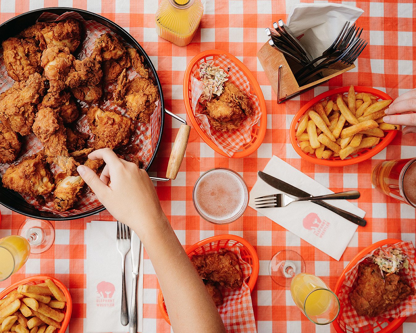 People reach for a big pan of fried chicken and chips on a checkered red tablecloth. One of the best bottomless brunches in Auckland.