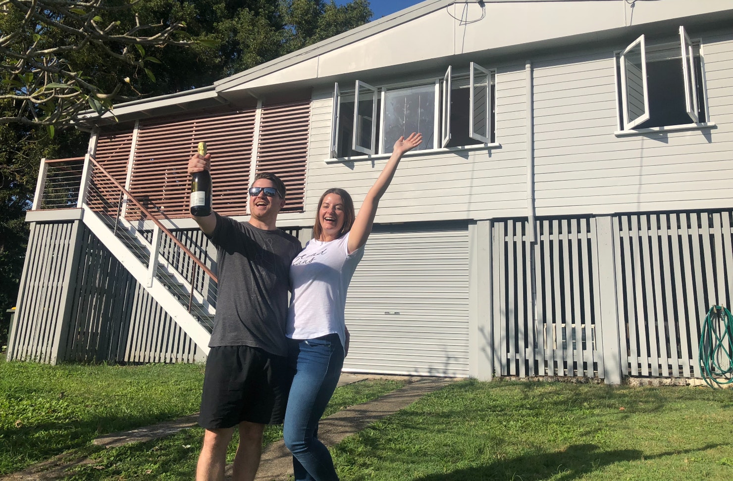 Couple standing outside a house holding a bottle of sparking wine