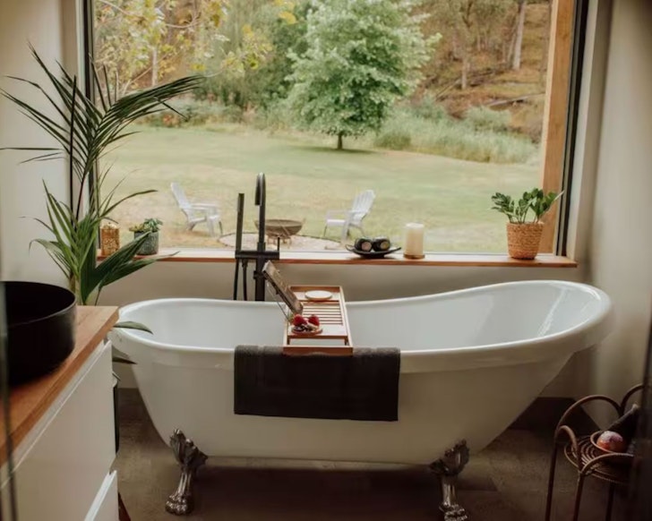The white claw foot bath in front of a window at Elm's Escape tiny home Victoria