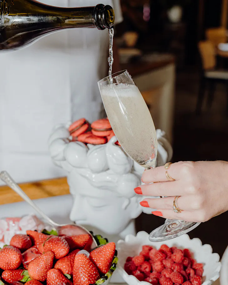 Someone with pretty manicured nails holds a flute while it's filled with champagne. 