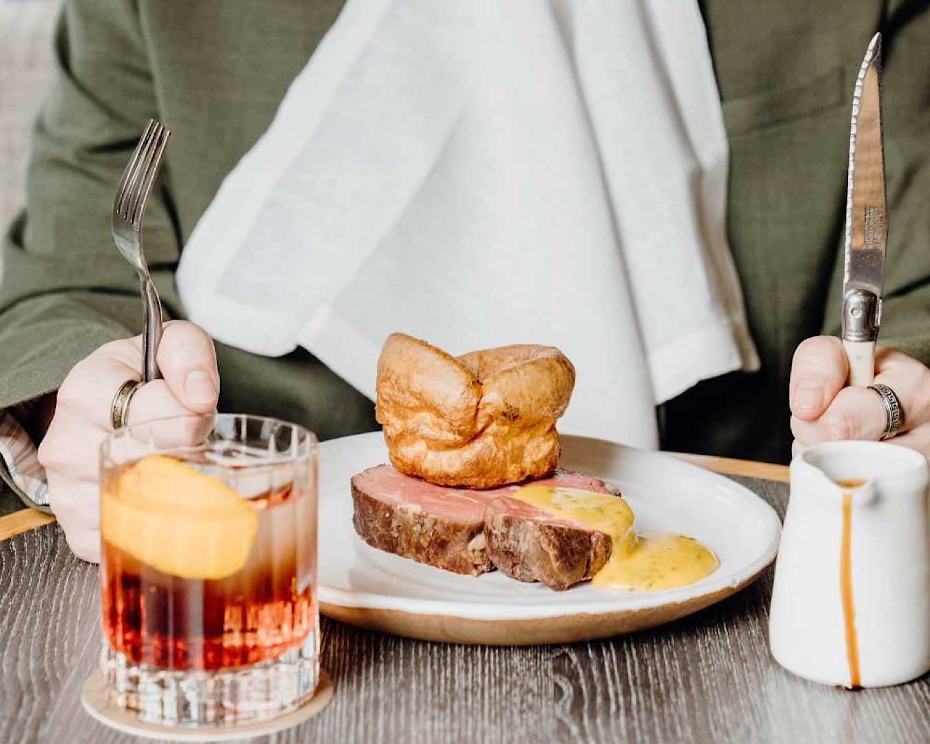 Somebody holds their knife and fork at the ready, about to dive into a slab of stake topped with yellow sauce and a large Yorkshire pudding at Esther Restaurant, one of the best places to go this Father’s Day. 