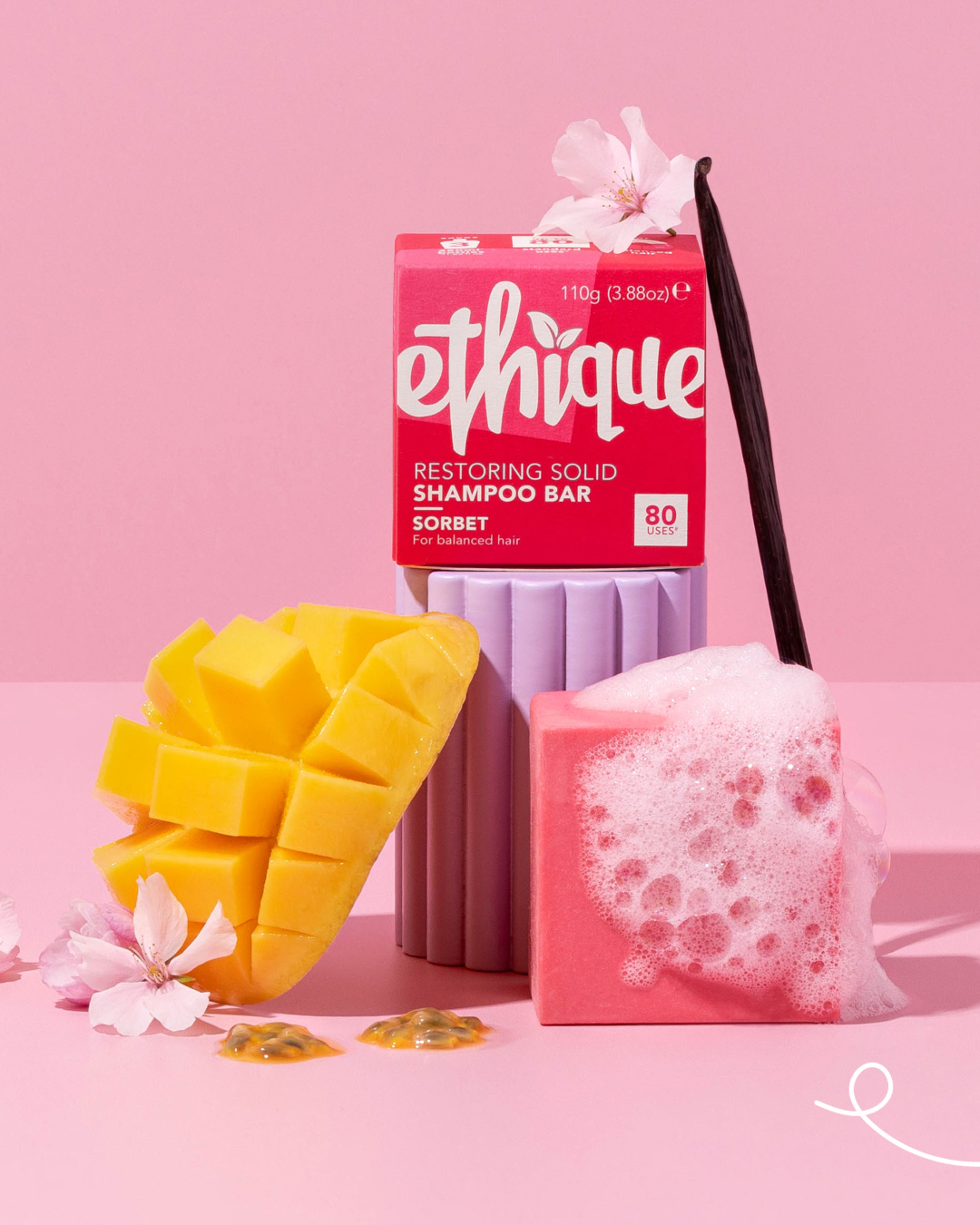 A hot pink soap box of Ethique sorbet shampoo with a square of foaming pink soap and mango styled against a light pink background.