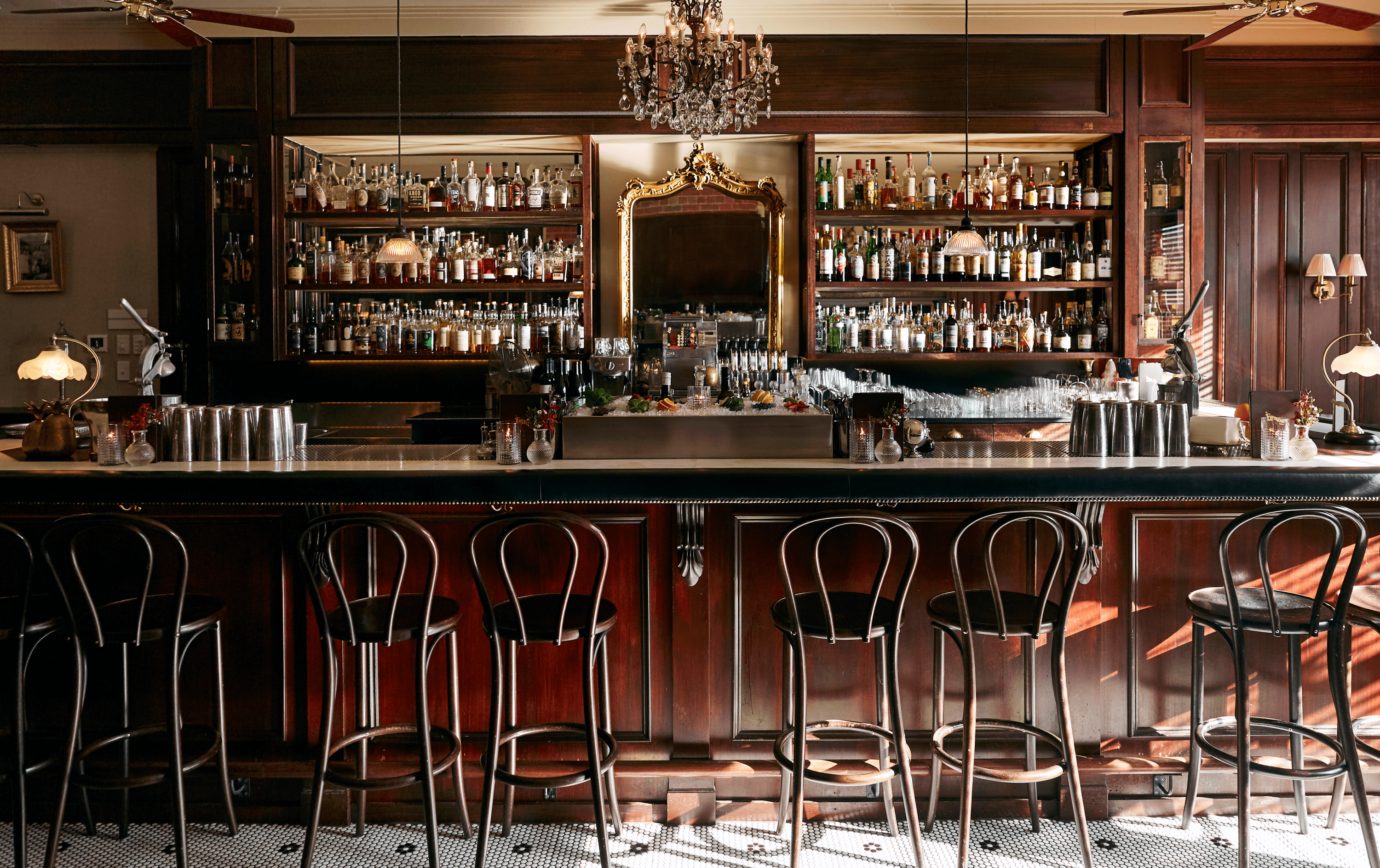 Arched bar stools lined at one of the best bars in Melbourne for 2023 with bottles lining the shelf. 