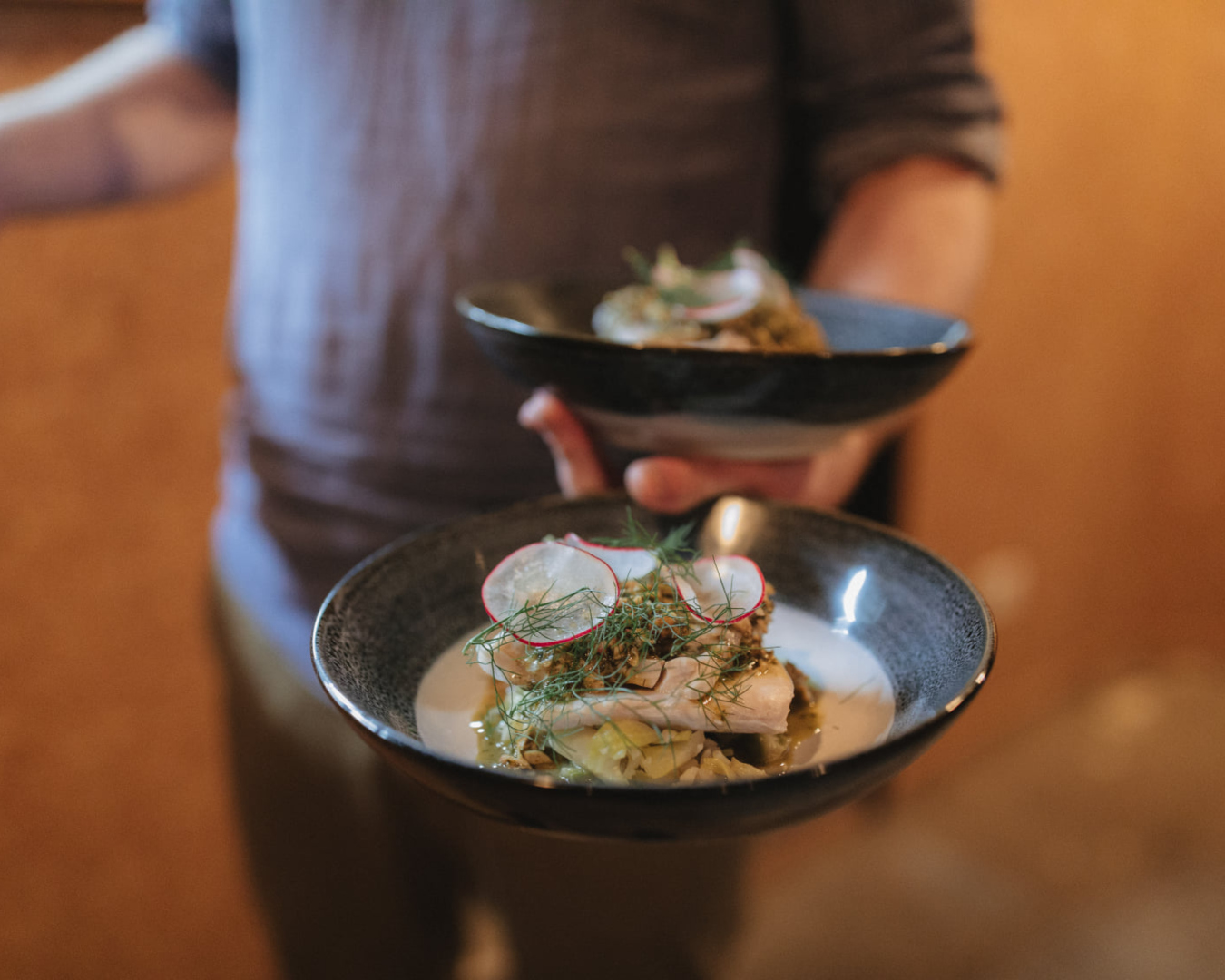 A person holds two dishes, each containing a delicious dinner prepared from food that would otherwise go to waste. 