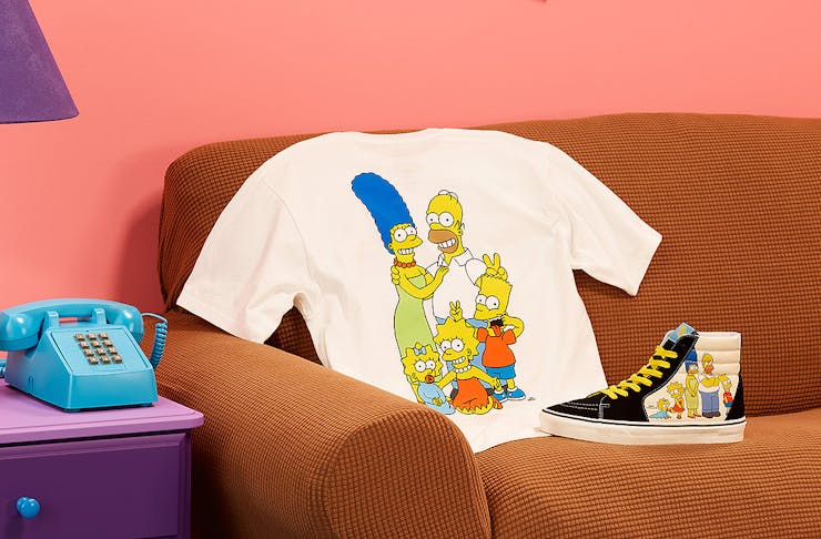 The Simpsons x Vans tshirt and Sk8-hi tops sit on The Simpson's couch.