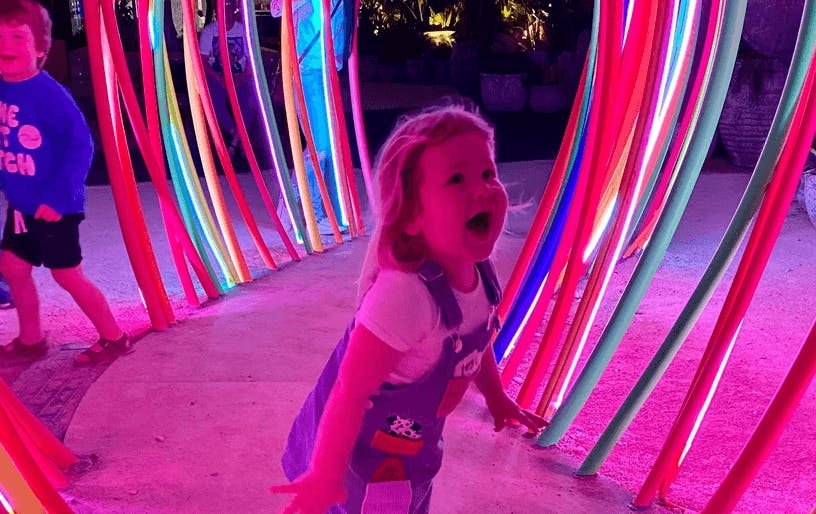 A small child playing inside a neon-lit installation. 