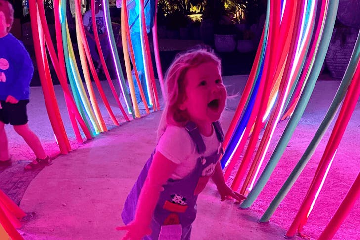 A small child playing inside a neon-lit installation. 