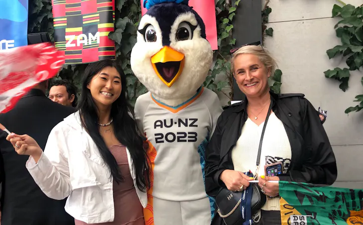 Two woman and the FIFA WWC mascot smile together