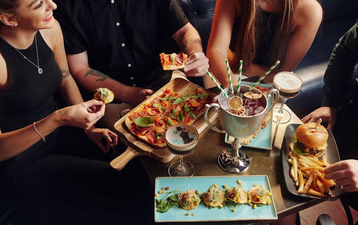 people enjoying food and drinks at Flight Club, including a giant cocktail in a trophy
